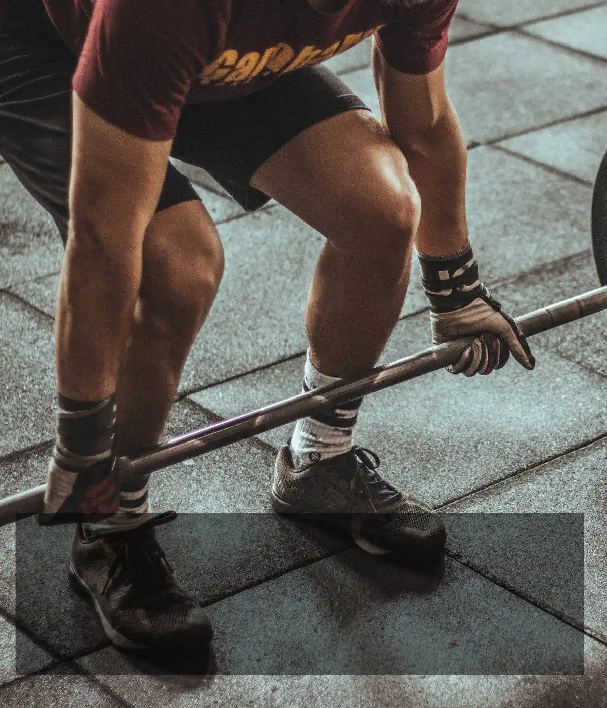 A weightlifter grips a barbell while wearing black shorts and striped socks.